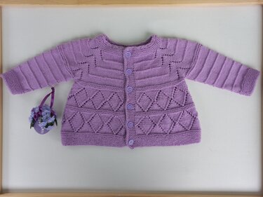 Fliederfarbene, gestrickte Babyjacke mit Knopfleiste und Rautenmuster, flach liegend fotografiert