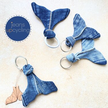 Four whale-tail keychains made from blue denim on a light background; one has a white ring and one includes a wooden tag.