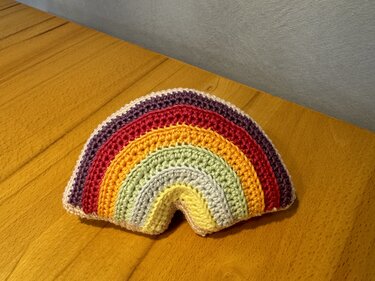 Gehäkelter Regenbogen mit bunten Streifen auf Holztisch