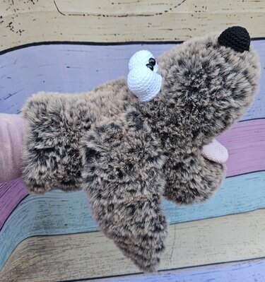 Nahaufnahme brauner flauschiger Amigurumi-Handpuppe mit weißen gehäkelten Augen, schwarzer Nase und rosa Zunge