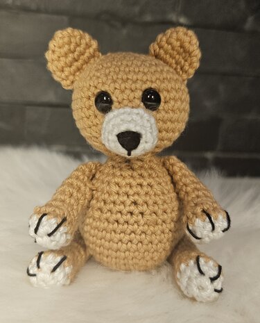 Beiger gehäkelter Teddybär mit weißen Pfoten und schwarzer Nase frontal sitzend