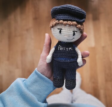 Hand hält gehäkelte Amigurumi-Puppe in dunkelblauer Polizeiuniform mit Mütze