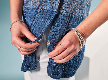 Hände schließen Knopf an blauem, dezent glitzerndem Strickcardigan