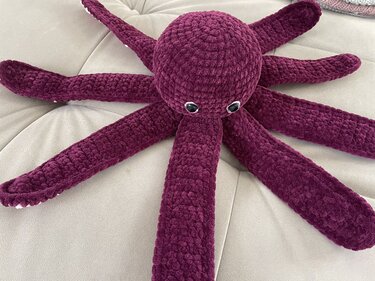 Weinroter gehäkelter Oktopus mit acht Tentakeln auf hellem Sofa
