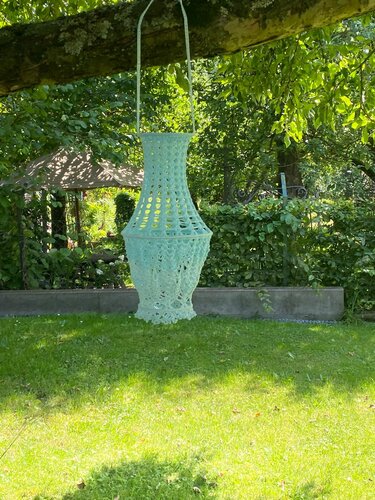 Mintgrüne, gehäkelte Hängedeko mit offenem Maschenmuster hängt an einem Baum
