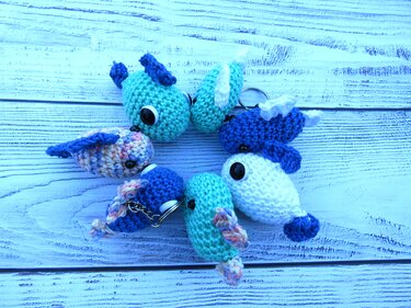 Sechs gehäkelte Amigurumi-Fische in Blau-, Türkis- und Weißtönen als Schlüsselanhänger auf hellem Holzhintergrund