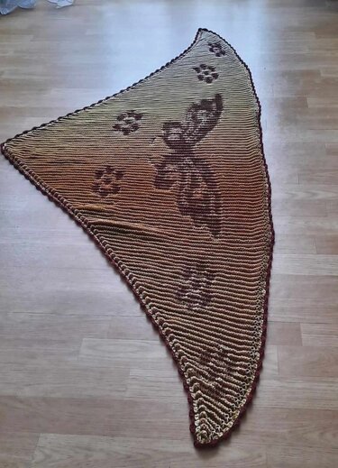 Gestricktes Dreieckstuch in Brauntönen mit Schmetterlings- und Pfotenmotiven auf hellem Holzboden