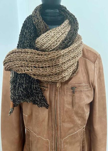 Langer gehäkelter Schal in melierten Braun-, Beige- und Schwarztönen, mehrfach um den Hals einer Schaufensterpuppe gewickelt.