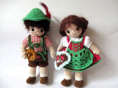 Zwei gehäkelte Amigurumi-Puppen in Tracht, Junge mit Hut und Brezel, Mädchen im Dirndl mit Herztasche.