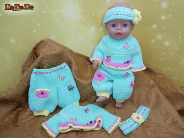 Babypuppe trägt mintfarbenen gehäkelten Pullover, passende Hose und Stirnband, zusätzliches Set neben der Puppe auf braunem Stoff