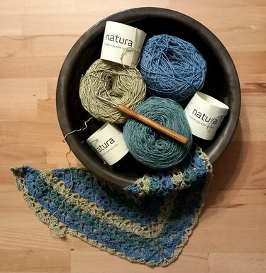 Schale mit Garnknäueln, Häkelnadel und halbfertigem blau-grünem Dreieckstuch