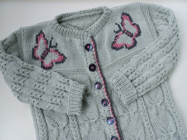 Hellgraue gestrickte Babyjacke mit rosa-schwarzen Schmetterlingen und dunklen Knöpfen