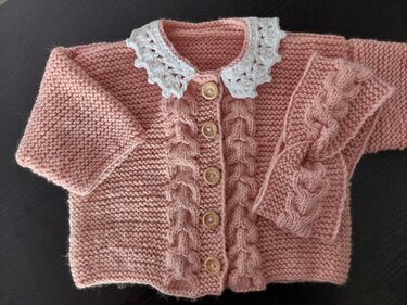 Rosa gestrickte Babyjacke mit weißem Häkelkragen, Holzknöpfen und Zopfmuster‑Stirnband