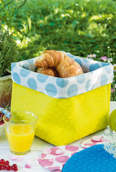Gelbes Stoffkörbchen mit blau-weißem Punkte-Umschlag, darin Croissants