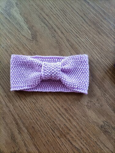 Helllila gestricktes Stirnband mit mittigem Knoten auf Holzuntergrund