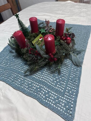 Kühler blauer Häkel-Tischläufer unter Adventskranz mit vier roten Stumpenkerzen