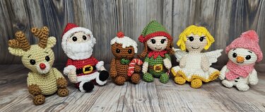 Sechs gehäkelte Amigurumi-Weihnachtsfiguren auf Holzuntergrund: Rentier, Weihnachtsmann, Lebkuchenmännchen, Elf, Engel und Schneemann.