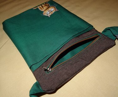 Grüne Stofftasche mit orangefarbenem Cartoon-Katzenmotiv und braunem Reißverschlussfach