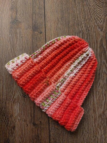 Handgehäkelte Mütze in Orange, Rosa und Grün auf Holz