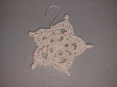 Weißes gehäkeltes Sternornament mit Aufhängeschlaufe auf grauem Hintergrund