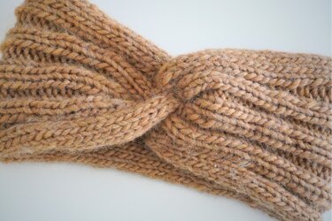 Nahaufnahme eines beigen Rippenstrick-Stirnbands mit gedrehtem Knoten