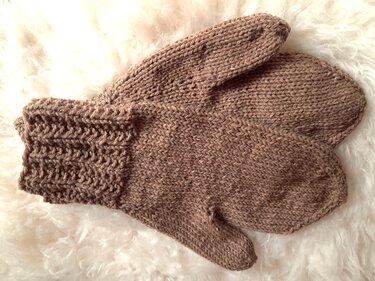 Zwei braune Fäustlinge mit Rippenbündchen auf hellem, flauschigem Untergrund