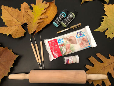 Auswahl an Modelliermaterialien (Modelliermasse, Werkzeuge, Farben, Nudelholz) auf dunklem Untergrund mit Herbstblättern