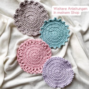 Vier gehäkelte runde Untersetzer in Pastellfarben auf hellem Stoff