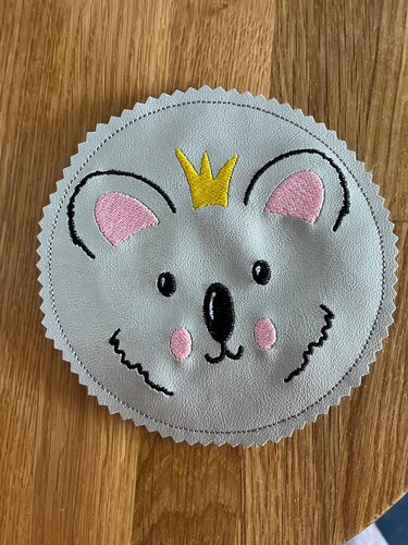 Runde Koala-Applikation mit gelber Krone, rosa Ohren und Wangen auf hellem Holz