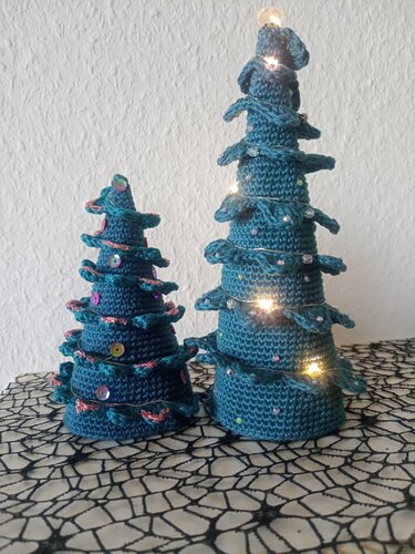 Zwei gehäkelte Weihnachtsbäume in Türkis, einer mit Lichterkette, der andere mit pinken Akzenten und Pailletten