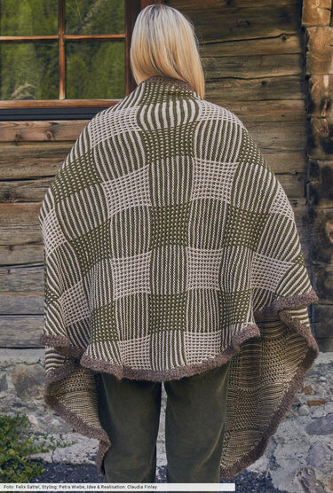 Rückenansicht einer Person mit hellem Haar, die einen gestrickten Poncho mit grün-beigem Schachbrettmuster und dunkelbrauner Kante trägt.