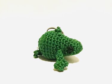 Gehäkelter grüner Amigurumi‑Frosch mit Schlüsselring vor weißem Hintergrund
