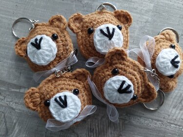 Fünf gehäkelte braune Teddybär-Schlüsselanhänger mit weißen Schnauzen und Schleifen auf grauem Holz.
