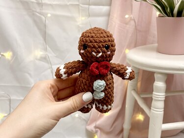 Gehäkelter Lebkuchenmann mit roter Schleife und hellblauen Knöpfen, von Hand gehalten