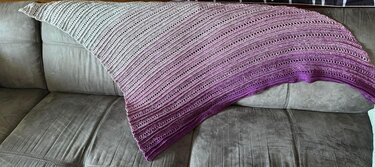 Handgehäkeltes Dreieckstuch mit diagonalem Lochmuster, Farbverlauf Hellgrau zu Lila auf Sofa