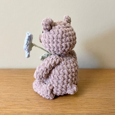Rückenansicht: sitzender gehäkelter Teddy in zartrosa mit Blume