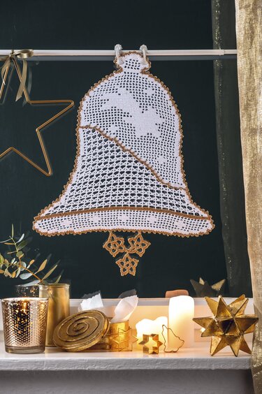 Weiße Häkelglocke mit goldener Umrandung vor dunklem Fenster, dekorativ mit Kerzen arrangiert