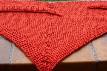 Nahaufnahme eines roten gestrickten Dreieckstuchs mit Krausrippenmuster auf Terrakottafliesen