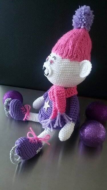 Gehäkelter Amigurumi-Teddy sitzend mit rosa Bommelmütze und lila Outfit