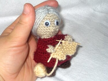 Kleine gehäkelte Großmutter Figur mit Strickzeug, in einer Hand gehalten, detailliert.