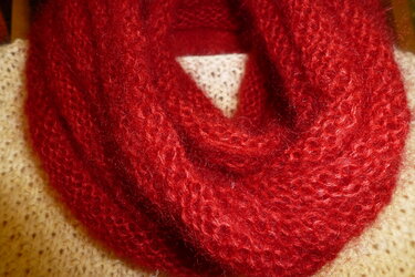 Nahaufnahme eines roten, flauschigen Loop‑Schals auf hellem Strickpullover.