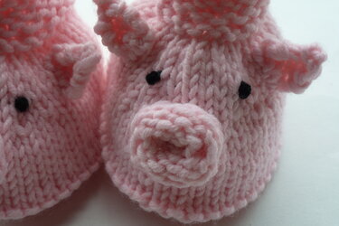 Nahaufnahme eines rosa gestrickten Babyschuhs mit aufgesetzter Schnauze und schwarzen Augen
