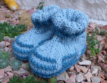 Nahaufnahme gestrickter hellblauer Babyschuhe mit sichtbarer Maschenstruktur