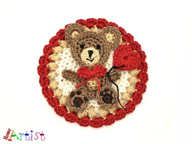 round crochet applique of teddy bear holding a red heart on scalloped red and cream background