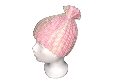 Seitenansicht einer gehäkelten Mütze in Rosa, Beige und Weiß mit dekorativem Knoten auf einer weißen Büste.