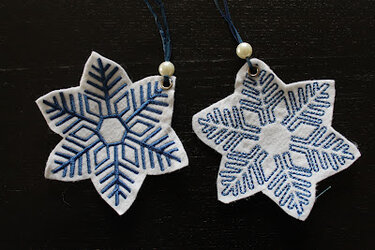 Nahaufnahme zweier weißer Filz-Schneeflocken mit unterschiedlichen blauen Stickmustern und Aufhängungen