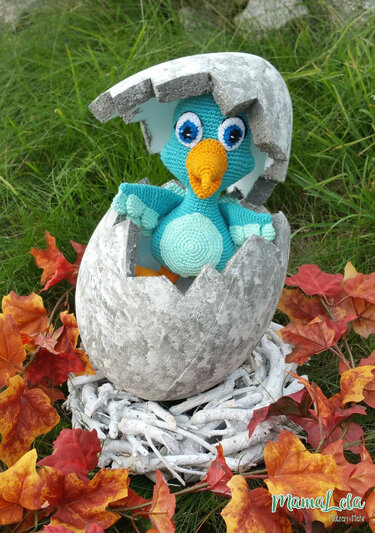 Türkis gehäkeltes Amigurumi-Vogelbaby in zerbrochener Eierschale zwischen Herbstlaub