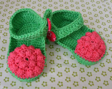 Grüne gehäkelte Babyschuhe mit pinker, strukturierter Zehenkappe und Riemchen mit rotem, gepunktetem Knopf