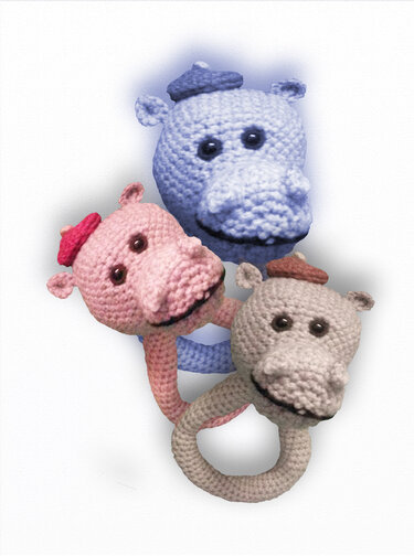 Nahaufnahme von drei gehäkelten Nilpferd-Rasseln in Blau, Rosa und Beige mit kleinen Baretten