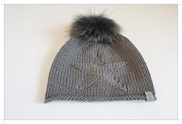 Graue Strickmütze mit Sternmuster und großem flauschigem Bommel auf weißem Hintergrund.